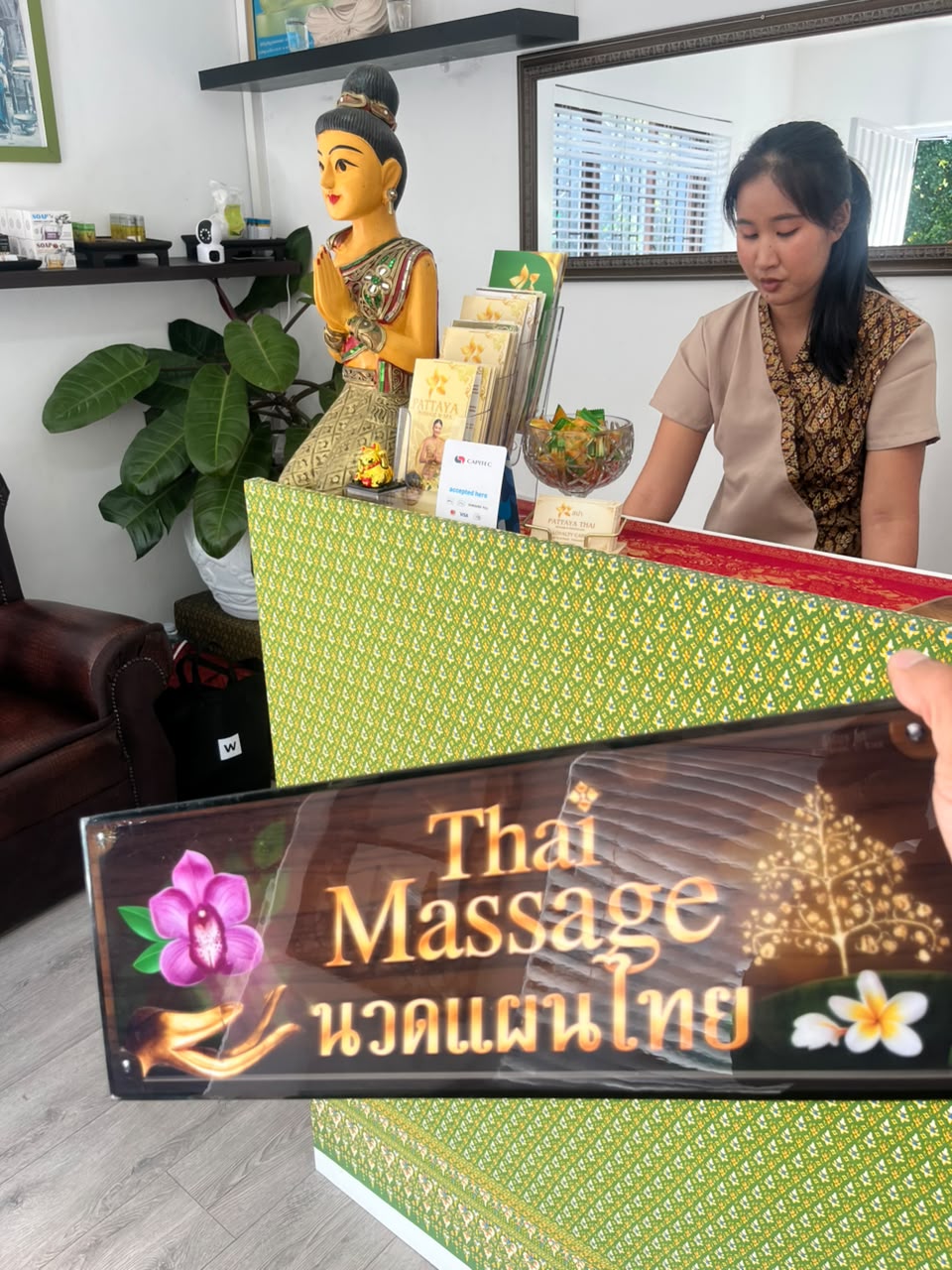 Reception welcome Thai therapist welcoming guests at the green patterned reception desk