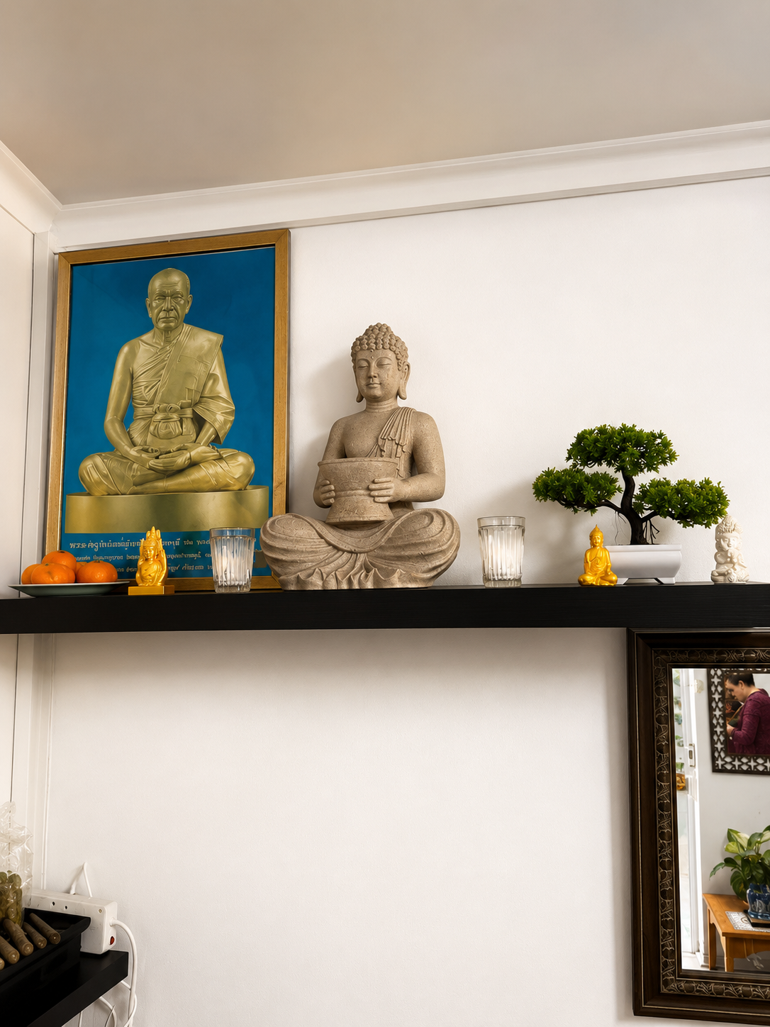 Buddha shrine shelf Stone Buddha statue, gilded monk portrait and bonsai arranged on a dark shelf above the spa waiting area